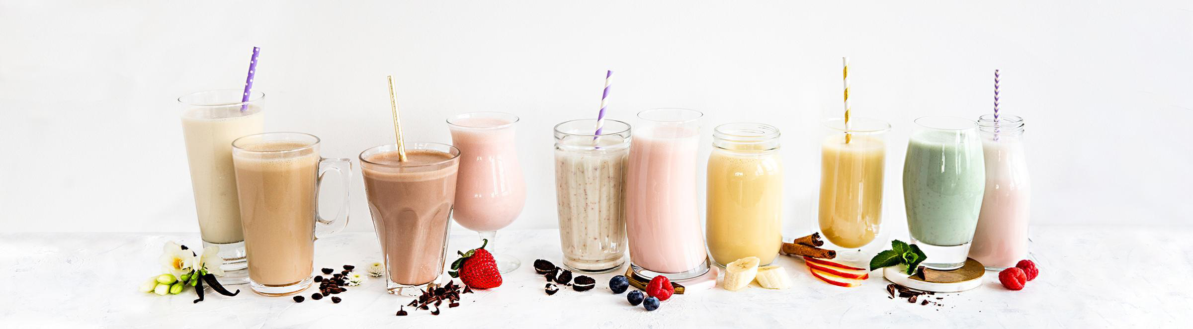 Row of colorful milkshakes in glasses with straws on a white background
