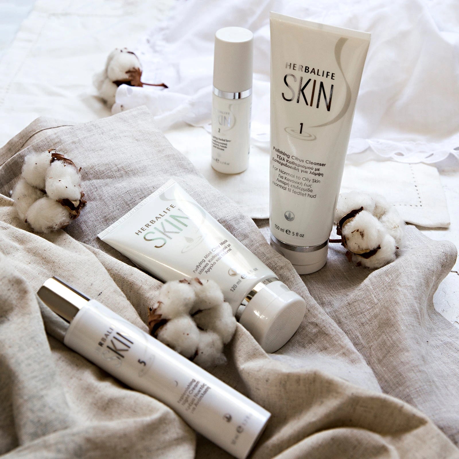 Herbalife Skin skincare products on a textured surface with cotton fibers.